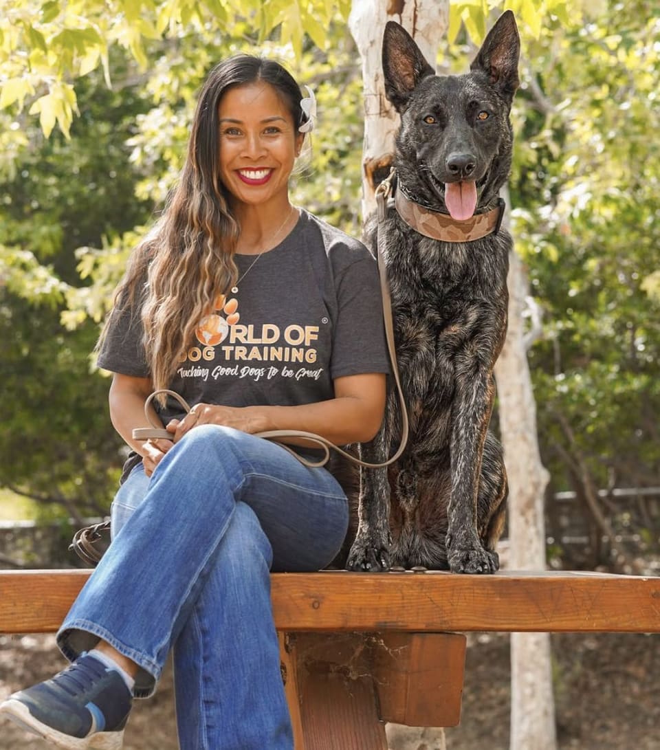 Kim seated on a bench beside Vader, her brindle Dutch Shepherd, leash loose in her hands